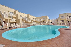 A swimming pool with a curved edge, surrounded by lounge chairs and a white fence. - Vacation Apartment 'Marysol' with Shared Pool, Private Terrace and Wi-Fi (Caleta de Fuste)