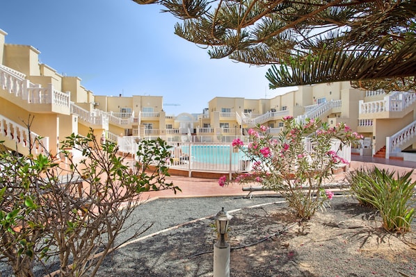 A hotel courtyard with multiple balconies, a swimming pool, and various plants.