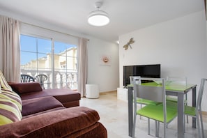 A living room with a sofa, a dining table with chairs, a TV, and a window with curtains.