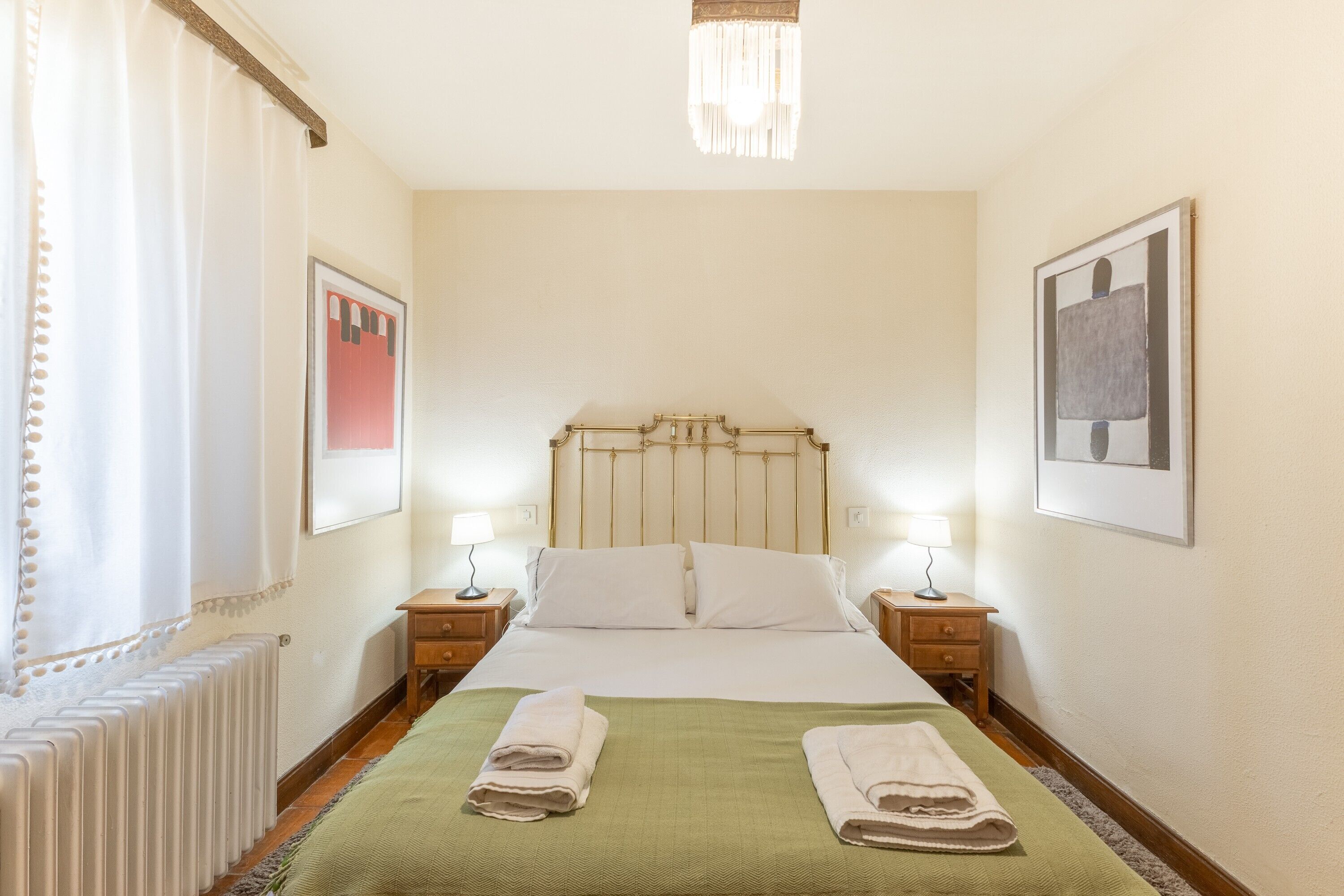 Quarto de hotel com cama, duas mesas de cabeceira, um radiador e duas luminárias na parede.