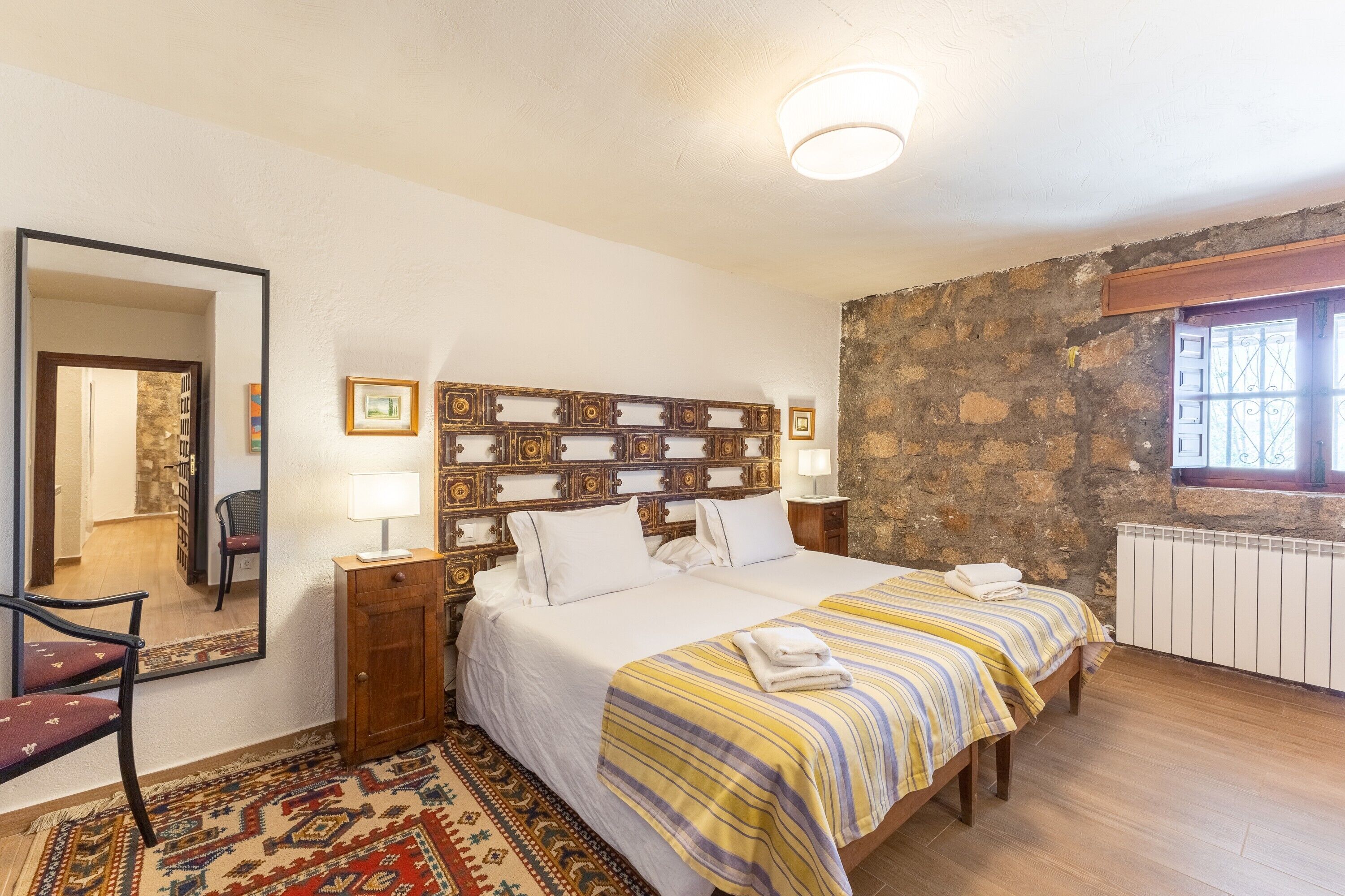 Quarto com cama grande, espelho, cabeceira de madeira, janela com grades e radiador.