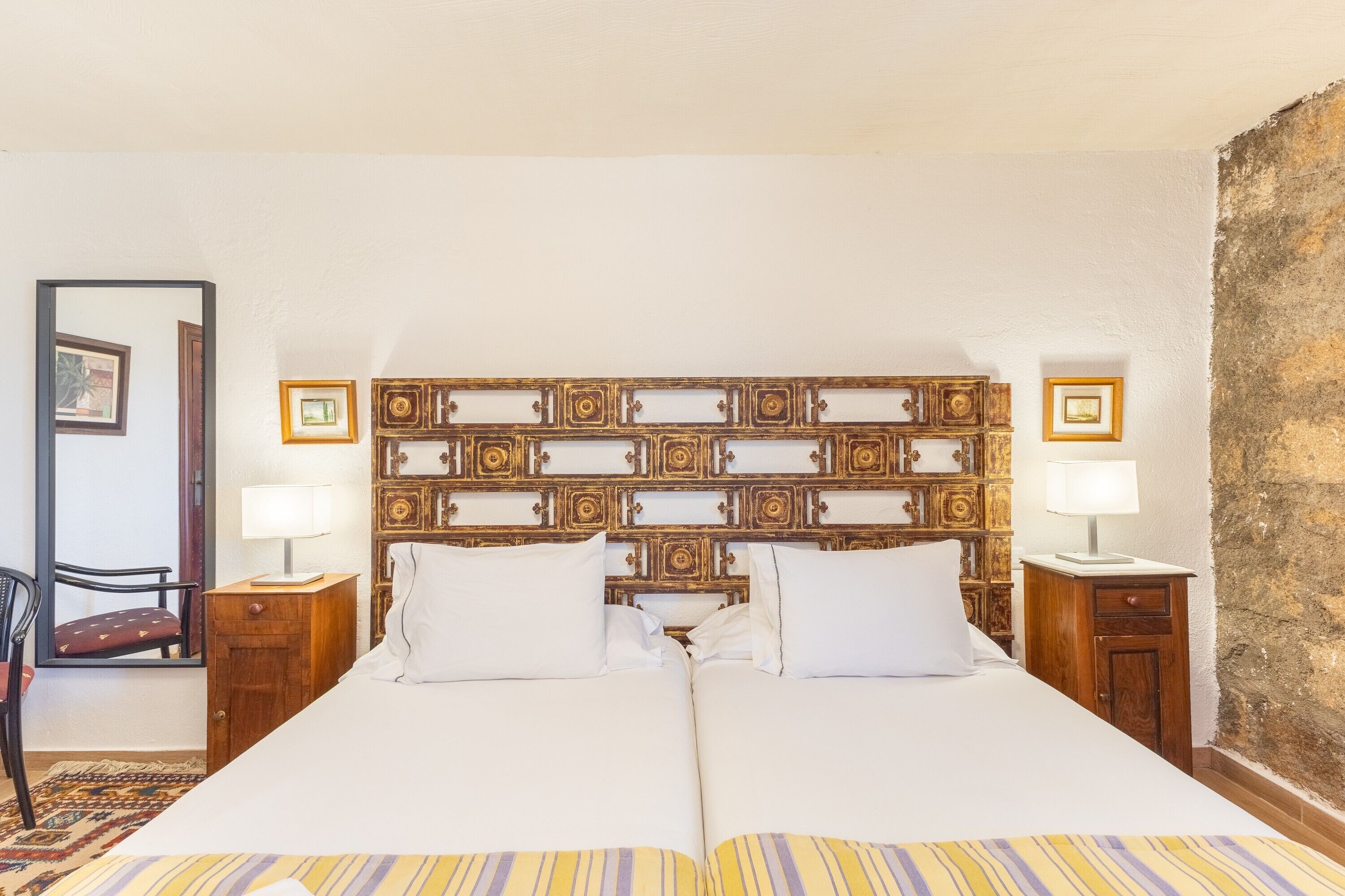 A double bed with a wooden headboard, two bedside tables with lamps, a chair, and a patterned rug.