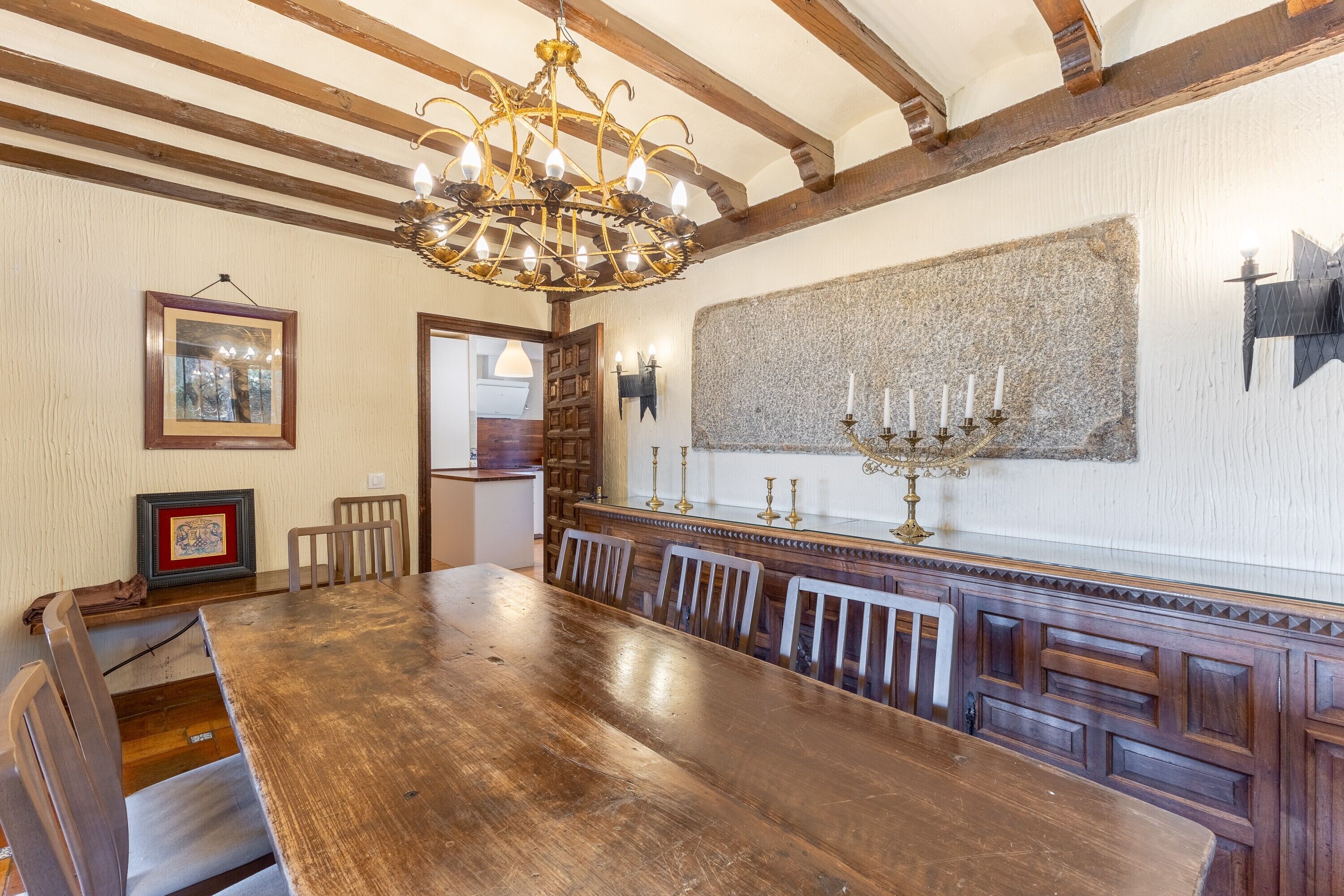Une salle à manger avec une grande table en bois, des chaises, un lustre et un mur en pierre.