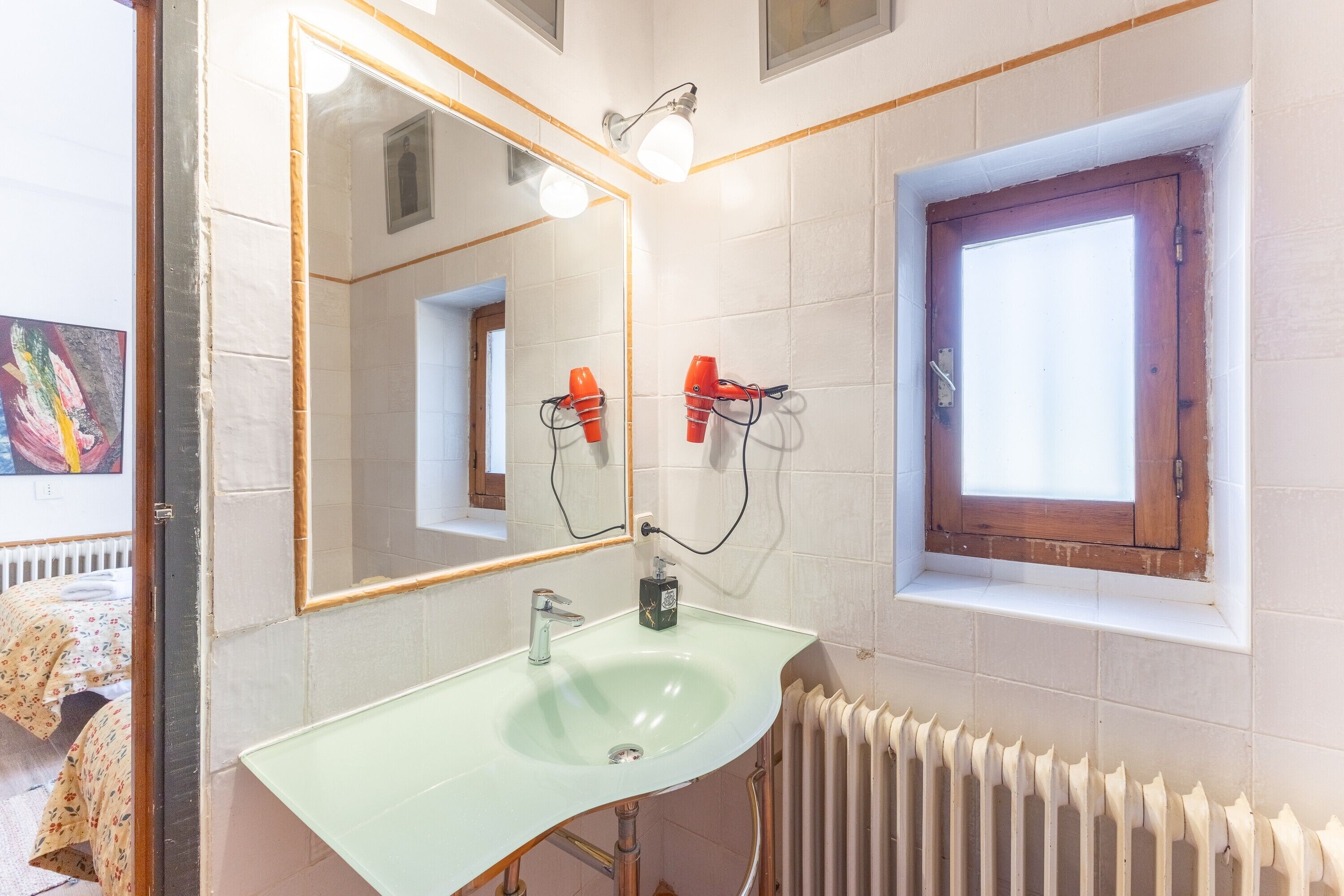 Une salle de bain avec un grand miroir, un lavabo vert clair, une porte en bois et un radiateur.