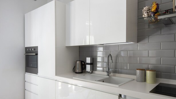 Een moderne keuken met witte kasten, een oven van roestvrij staal, een spoelbak en een betegelde spatwand.