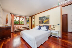 Une chambre à coucher avec un grand lit, une table de chevet, une commode, un banc et une fenêtre avec des rideaux.