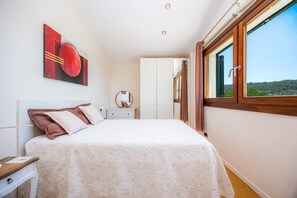A bedroom with a bed, a nightstand, a mirror, a window with curtains, and a painting on the wall.