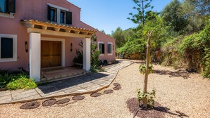 Un bâtiment rose doté d’un porche abrité, d’un chemin de gravier et entouré de verdure.
