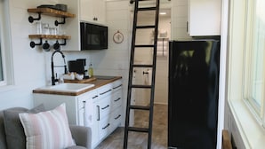 Una cocina pequeña con armarios blancos, un refrigerador negro, una encimera de madera y una escalera.