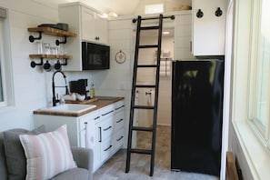 A compact kitchen with white cabinetry, a black refrigerator, a wooden countertop, and a ladder.