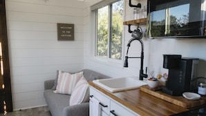 Una cocina compacta con encimera de madera, un lavabo, una cafetera y una ventana con vistas a árboles.
