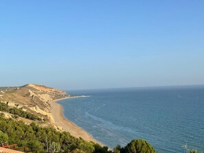 Un paisaje costero con una playa, una colina con una estructura en la cima y un cielo despejado.