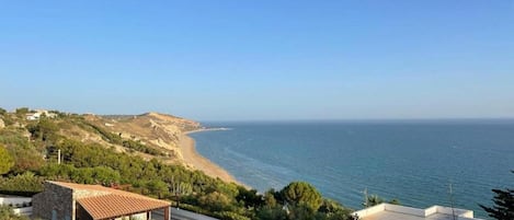 A coastal property with a view of the sea, a patio area, and a small building with a tiled roof.