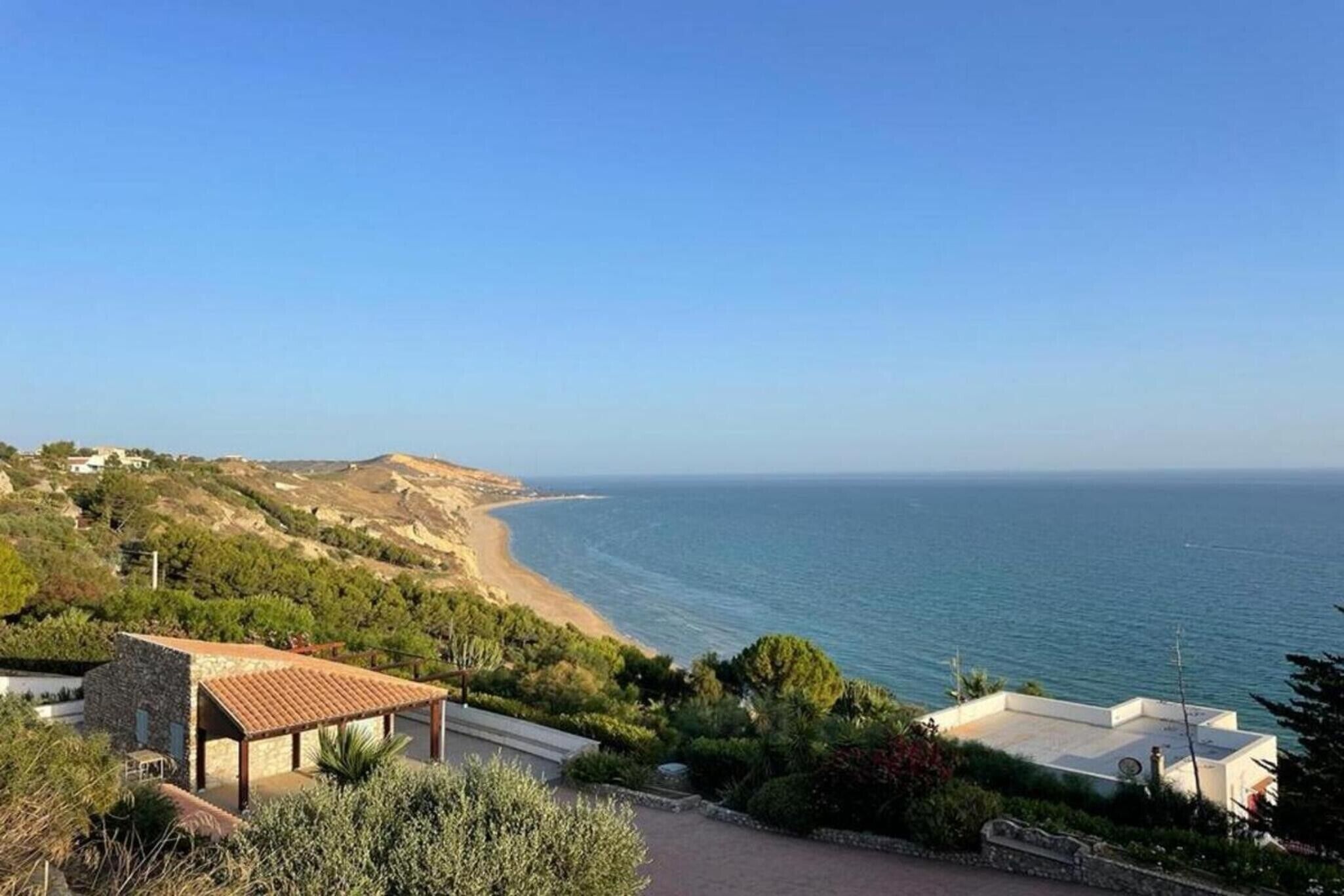 A coastal property with a view of the sea, a patio area, and a small building with a tiled roof.