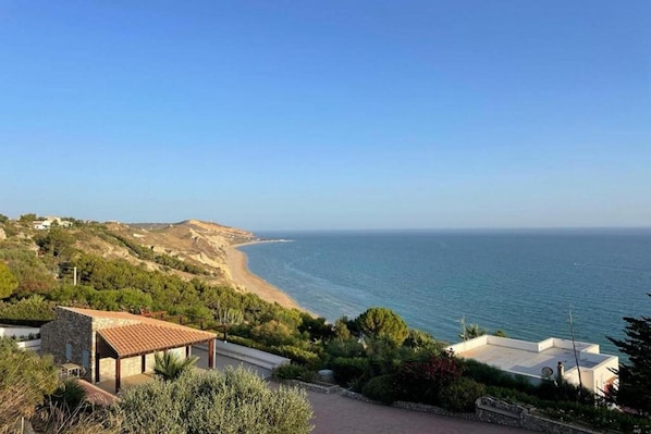 A coastal property with a view of the sea, a patio area, and a small building with a tiled roof.