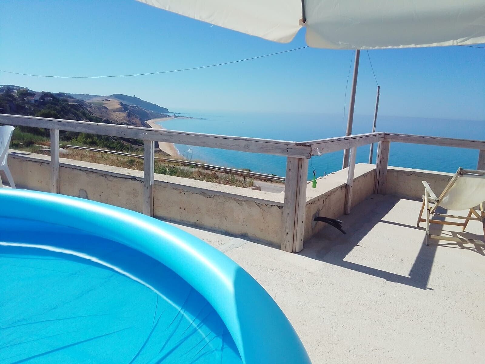 A pool with a view of the sea, a wooden deck, and a beach in the background.