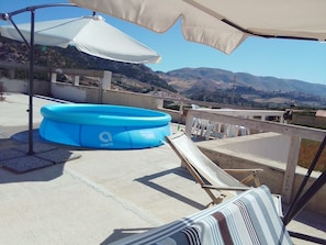 Un área de piscina al aire libre con piscina inflable azul, sillas de descanso y vistas del paisaje circundante.