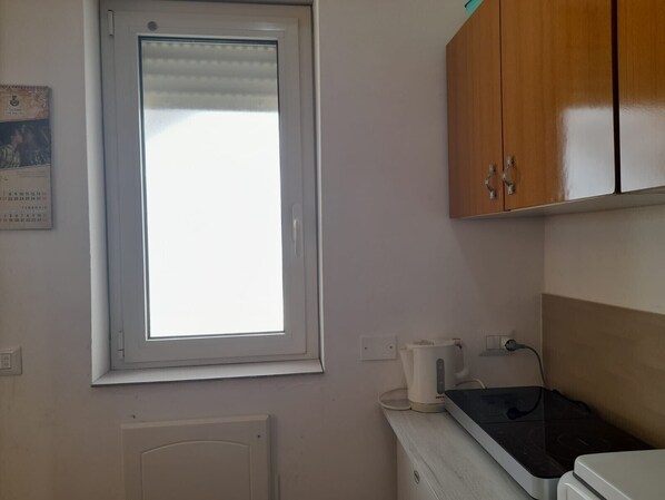 A kitchen with a window, a kettle, a toaster, and wooden cabinets.