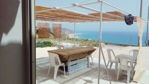 Une terrasse avec une table et des chaises, un espace abrité et une vue sur l’océan.