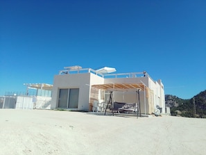 Un moderno edificio de dos pisos con un espacio exterior cubierto y una vista despejada del paisaje circundante.