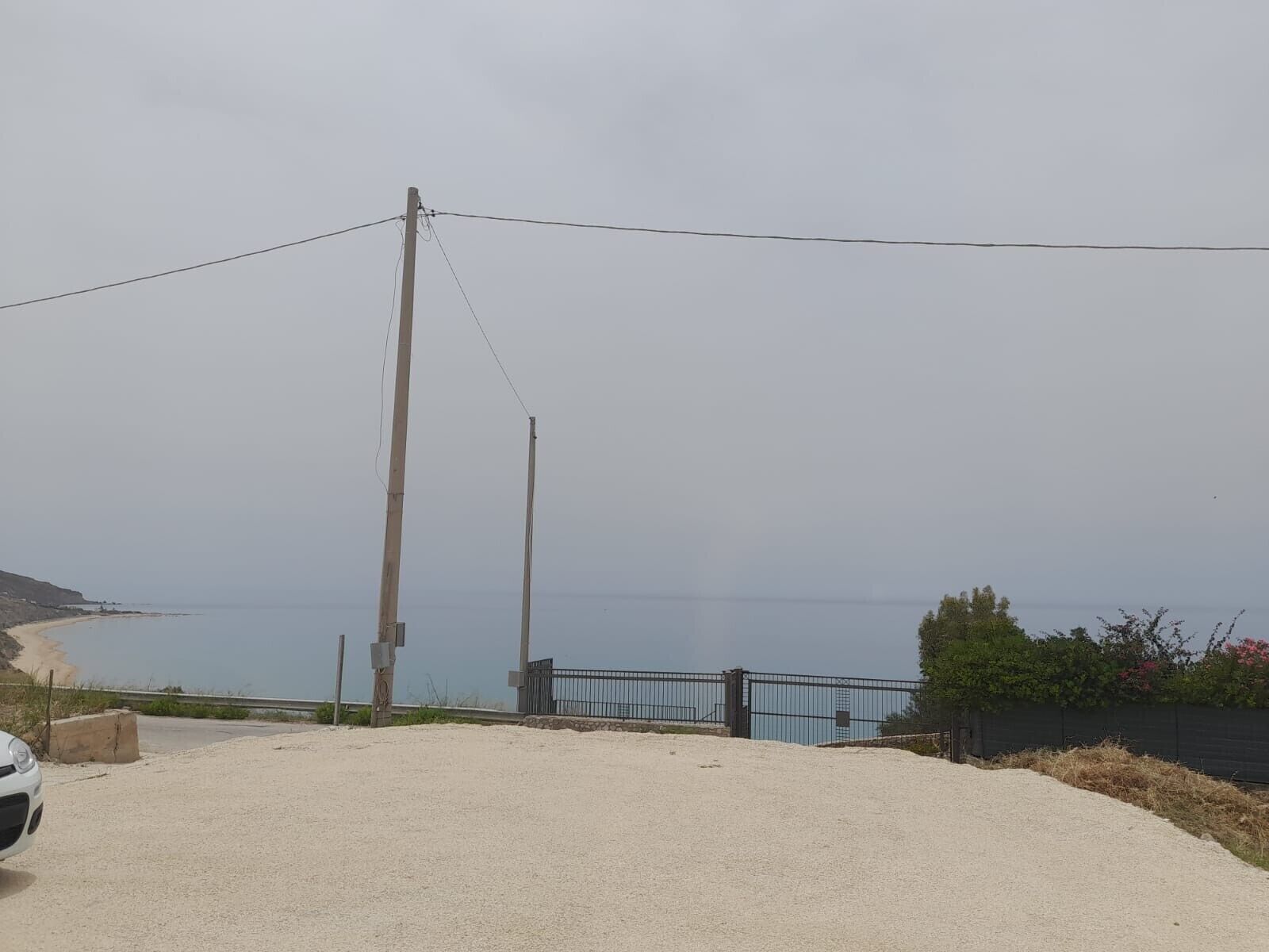 Un chemin de gravier menant à une entrée fermée par un portail, d’où l’on peut admirer la mer.