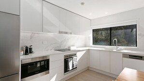 Una cocina moderna con armarios blancos, horno integrado, microondas y ventana con vista a árboles.