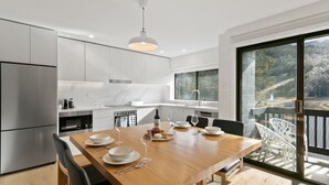 Una cocina moderna con armarios blancos, un salpicadero de mármol y un comedor con una mesa de madera preparada para cuatro personas.