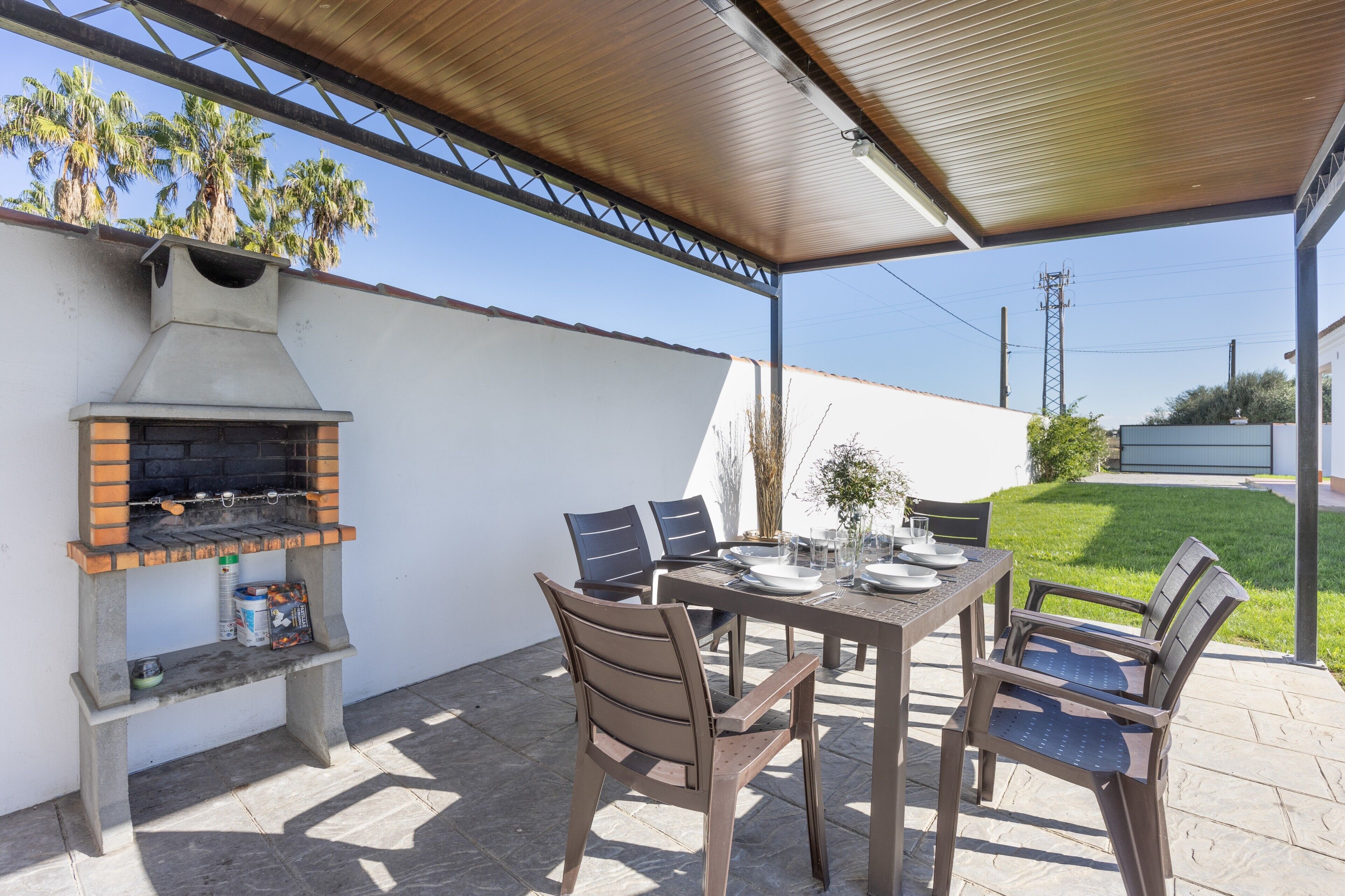 An outdoor patio with a brick grill, a table set for dining, and chairs.