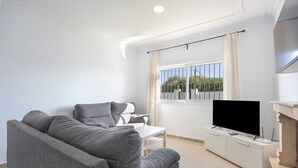 A modern living room with a grey sofa, a flat-screen TV, and a white coffee table.