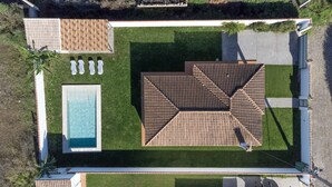 An aerial view of a property with a swimming pool, a patio area with chairs, and a large deck.