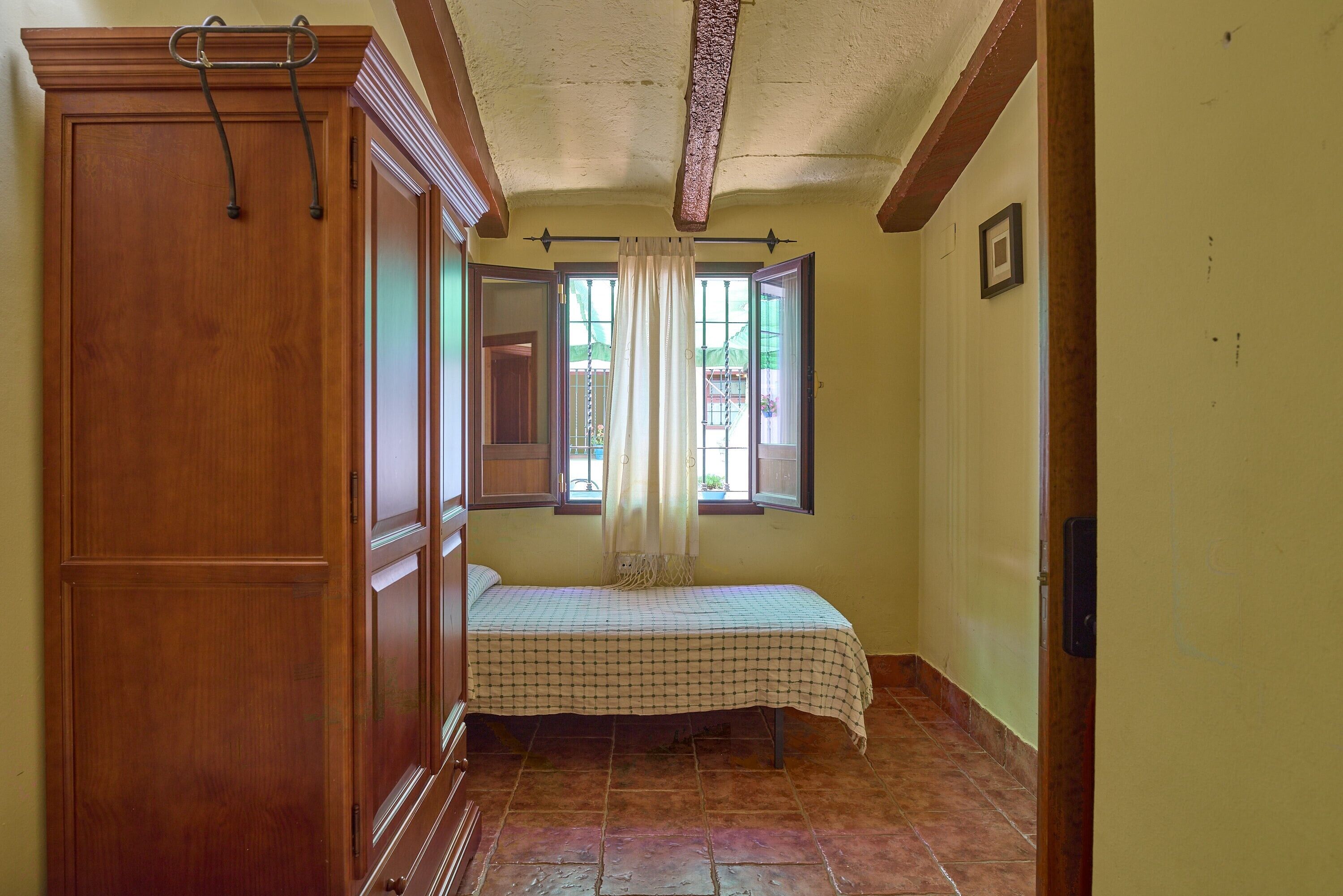 A room with a bed, wooden wardrobe, and a window with curtains.