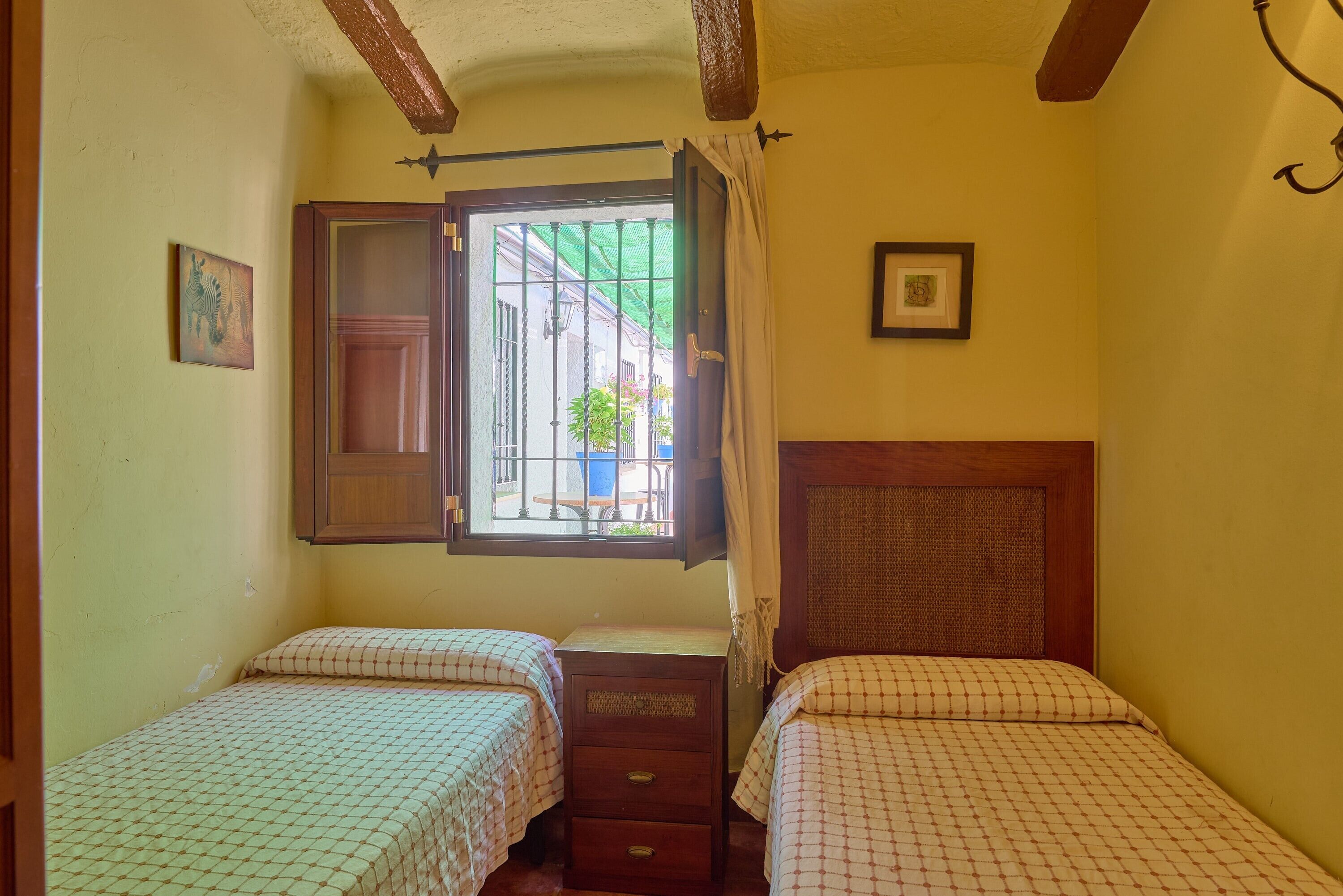 A room with two beds, a wooden headboard, a window with a view of the outside, and a door.