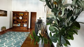 A room with a wooden floor, a patterned rug, a bookshelf, and a potted plant.