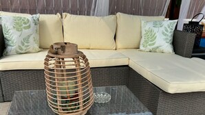 A glass-top coffee table with a woven wicker base, a metal lantern, and a cushioned sofa with patterned pillows.