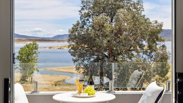 Un balcon avec une table dressée pour un repas, donnant sur un lac et des montagnes.