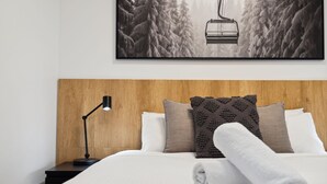 Un lit bien fait, avec une tête de lit en bois, une lampe de chevet et un tableau représentant un télésiège.