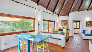 A dining area with a blue table and chairs, a kitchen area with a counter and chairs, and a living area with a sofa. - Villa 'Country House Sardinia' with Sea View, Wi-Fi and Air Conditioning (Olbia)