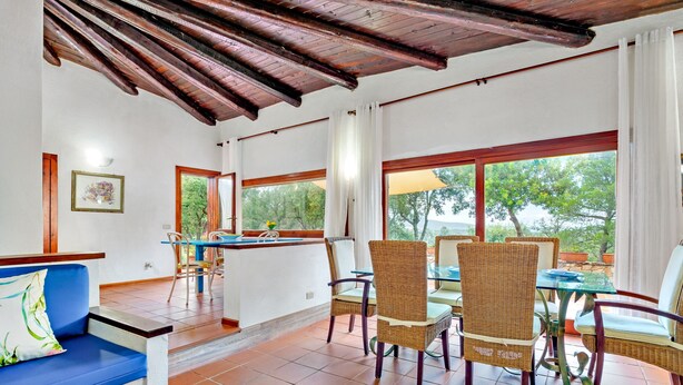 A room with a blue sofa, wicker chairs, a glass table, and large windows with a view of trees. - Villa 'Country House Sardinia' with Sea View, Wi-Fi and Air Conditioning (Olbia)