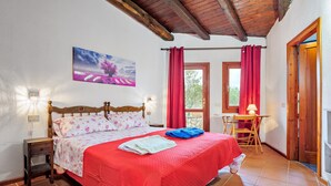 A bedroom with a bed, a nightstand, a chair, a table, and a painting on the wall. - Villa 'Country House Sardinia' with Sea View, Wi-Fi and Air Conditioning (Olbia)