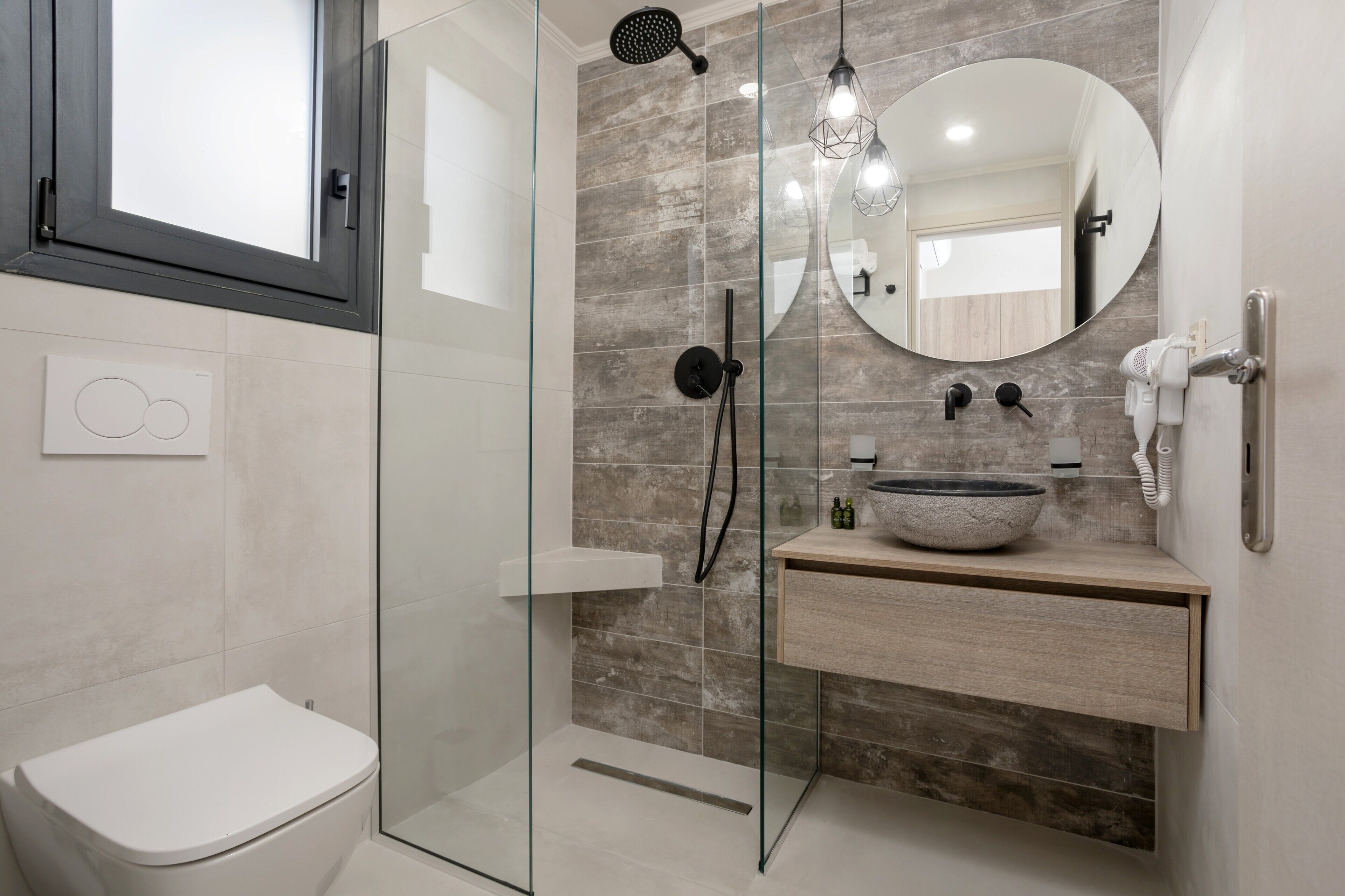 Ein modernes Badezimmer mit einer Duschkabine aus Glas, einer weißen Toilette, einem runden Spiegel und einem hölzernen Waschtisch mit Waschbecken.