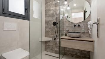 Ein modernes Badezimmer mit einer Duschkabine aus Glas, einer weißen Toilette, einem runden Spiegel und einem hölzernen Waschtisch mit Waschbecken.