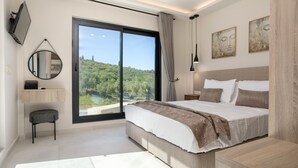 Quarto moderno com cama grande, vista para área verde através de uma porta deslizante, pequena escrivaninha e espelho.