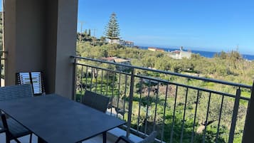 Ein Balkon mit Tisch und Stühlen, der auf eine Küstenlandschaft mit Bäumen und Gebäuden blickt.