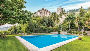 Une piscine rectangulaire bordée de pierres, entourée d’une pelouse bien entretenue et de différents arbres.