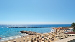 Une plage avec des parasols, des chaises longues et une jetée qui s’avance dans la mer.