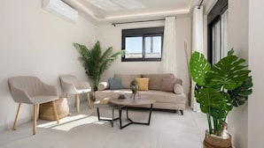 Ein modernes Wohnzimmer mit einer Couch, zwei Sesseln, einem Couchtisch und großen Kübelpflanzen.