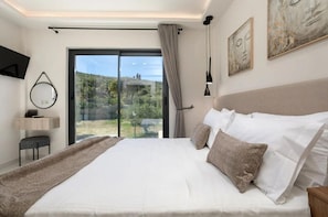 Een moderne slaapkamer met een groot bed, een bureau en uitzicht op een groen landschap door een schuifdeur.