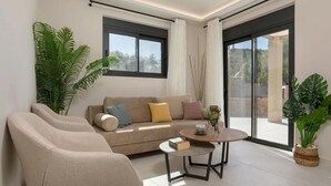 Ein modernes Wohnzimmer mit einer Couch, zwei Sesseln, einem Couchtisch und großen Fenstern.