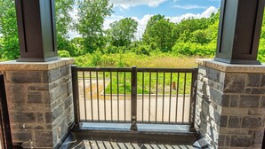 A covered outdoor area with stone pillars and a metal railing, overlooking a green landscape and a road. - Chic Retreat Near Niagara Falls (Niagara Falls)