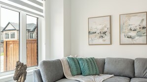 A living room with a grey sofa, two framed abstract paintings, a glass coffee table, and a horse sculpture. - Chic Retreat Near Niagara Falls (Niagara Falls)